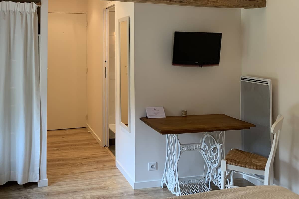 A room with exposed wooden beams, a television mounted on the wall, a sewing machine, and a small table with a chair.