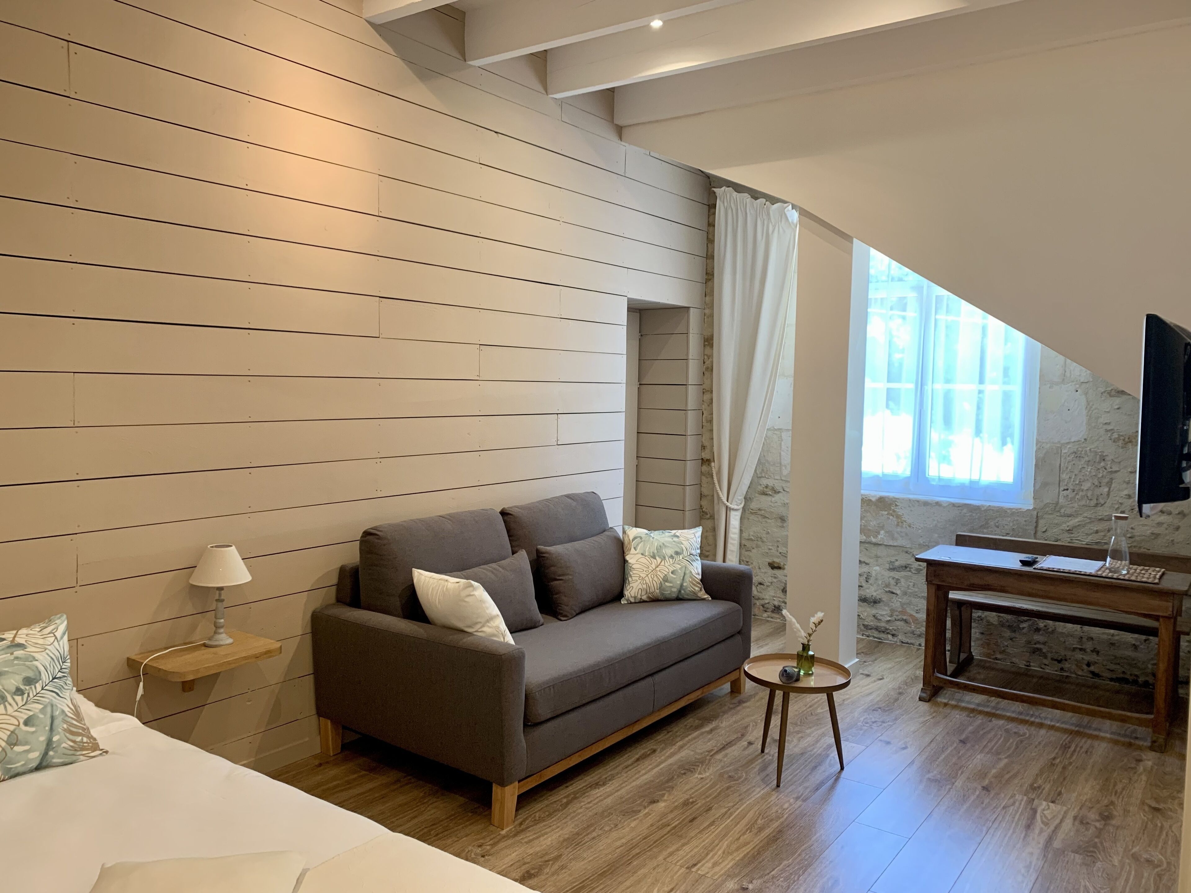 Una habitación moderna con un muro de listones de madera, un sofá gris, una pequeña mesa redonda con un florero y un banco de madera.