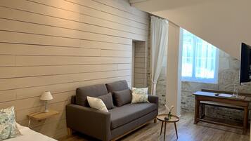 Una habitación moderna con un muro de listones de madera, un sofá gris, una pequeña mesa redonda con un florero y un banco de madera.