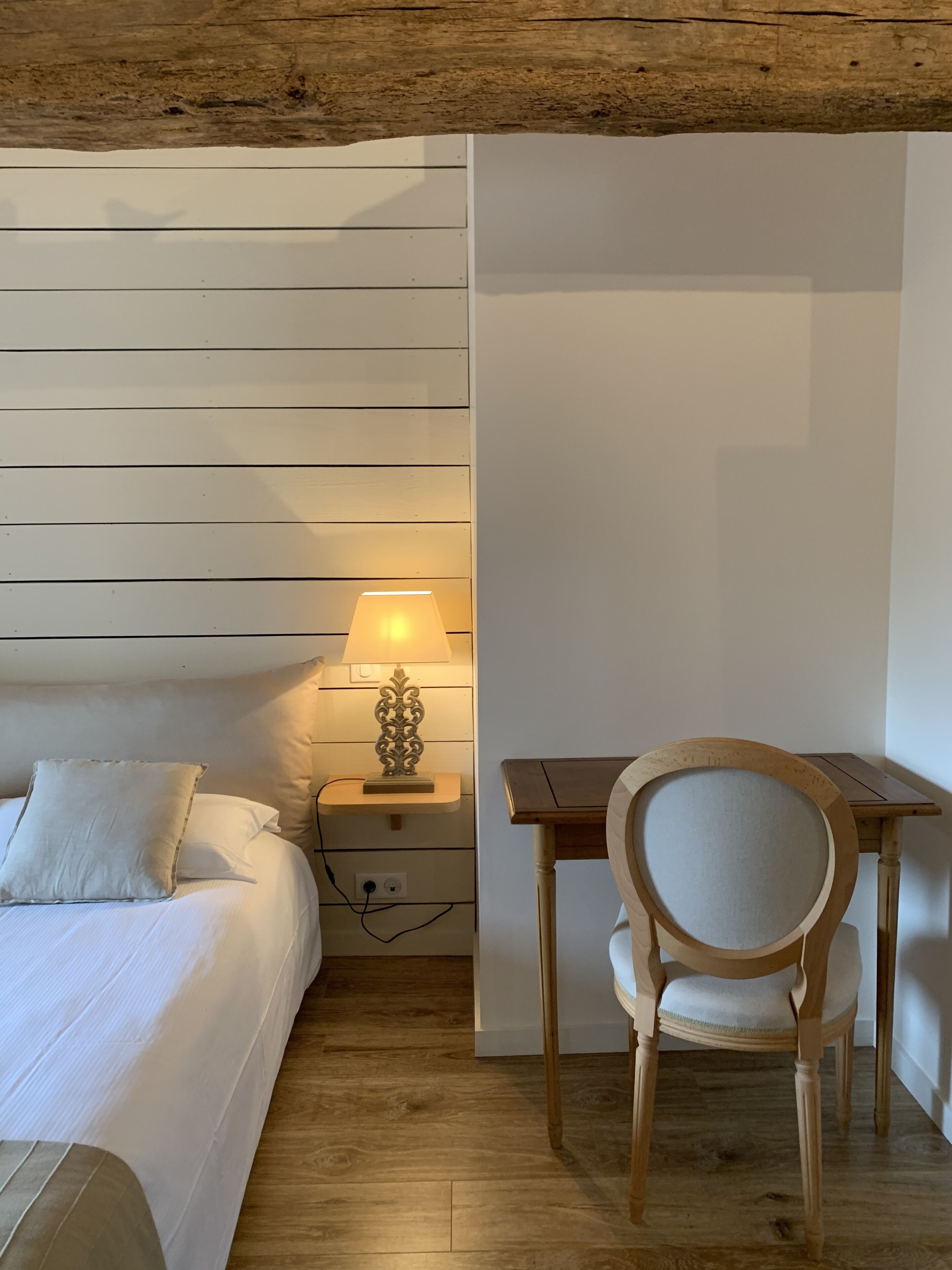 A bedroom with a bed, bedside table with a lamp, and a wooden chair.