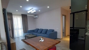 A modern living room with a wooden coffee table, a blue sofa, and a kitchen area with a black refrigerator. - Orexus Tower (Tbilisi)