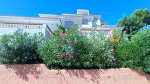 Un edificio blanco con techo de tejas, rodeado de exuberante follaje y plantas florecientes.