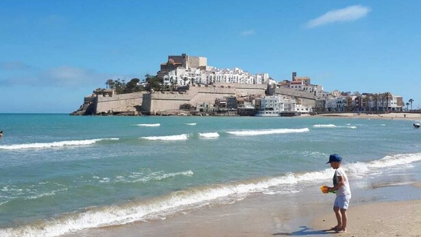 Una playa con un fuerte histórico y edificios blancos al fondo.