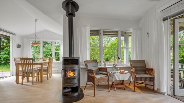 A cozy room with a wood-burning stove, wicker furniture, and large windows offering a view of greenery. - Awesome home in Malling with WiFi (Malling)