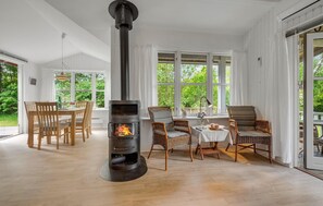 Una habitación acogedora con estufa de leña, muebles de mimbre y ventanas amplias con vistas a la vegetación.