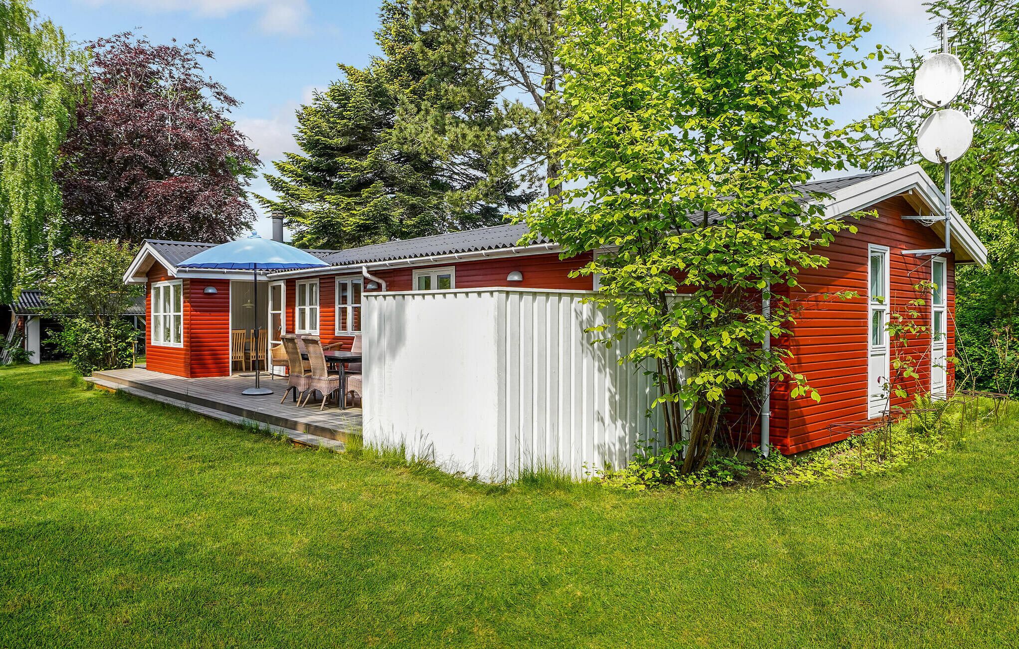 Une maison en bois rouge avec un patio couvert, une petite terrasse et une clôture blanche.