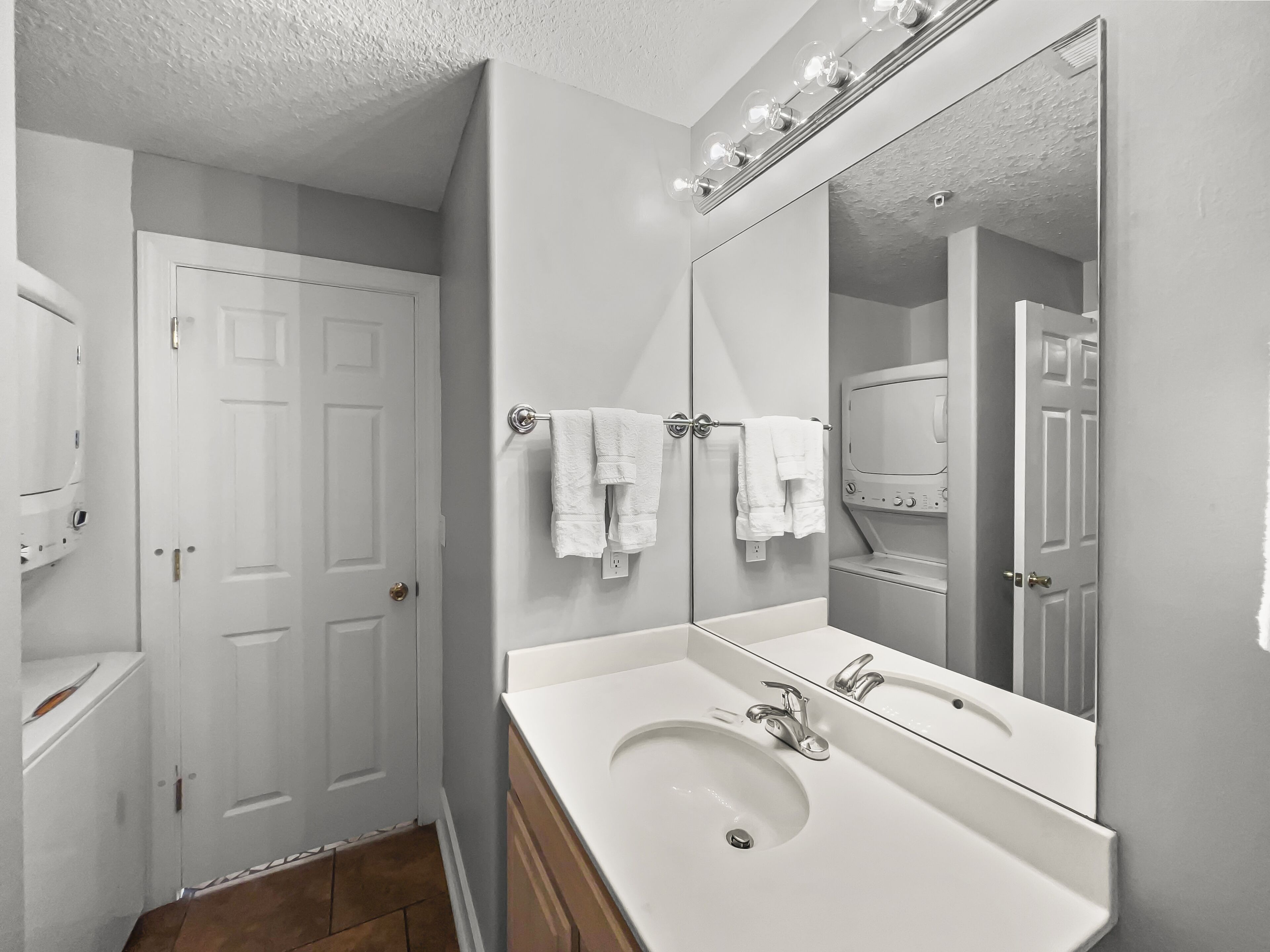 Une salle de bain avec un lavabo blanc, un grand miroir et un porte-serviettes sur lequel sont disposées plusieurs serviettes.