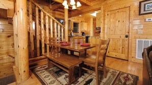 A wooden interior with a dining table set for four, a staircase, and a kitchen area. - Scenic Sunrise - Mountain Views + Community Pool Access + Outdoor Hot Tub (Sevierville)
