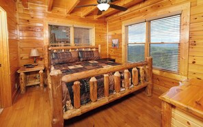 A log cabin bedroom with a wooden bed, a nightstand, a lamp, and a window with blinds.