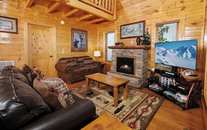 Un acogedor interior de cabaña de madera con chimenea, sofá de cuero y televisión.