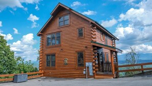 A log cabin with a balcony, a wooden fence, and a clear view of the mountains in the background. - Scenic Sunrise - Mountain Views + Community Pool Access + Outdoor Hot Tub (Sevierville)