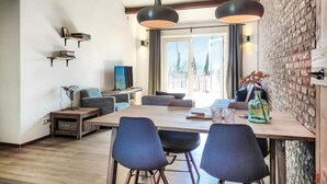 A dining area with a wooden table, four chairs, and pendant lighting. There is a television on a stand and a bookshelf with books. - 1 bedroom pet friendly home in Grashoek (Grashoek)