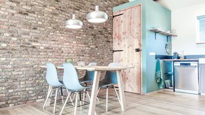 A dining area with a brick wall, a wooden door, and a kitchen with a dishwasher. - 1 bedroom pet friendly home in Grashoek (Grashoek)