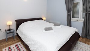 Una cama bien tendida con ropa blanca, un cabecero oscuro y dos lámparas de noche.