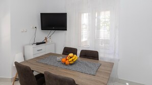 Un comedor moderno con una mesa de madera, cuatro sillas, un frutero y un televisor de pantalla plana montado en la pared.