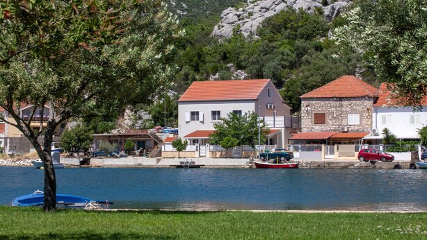 Un pueblo costero con casas frente al mar, una pequeña embarcación amarrada y una ladera rocosa al fondo.