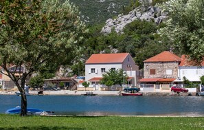 A coastal village with houses by the sea, a small boat docked, and a rocky hillside in the background. - Beautiful home in Rogotin with WiFi (Rogotin)