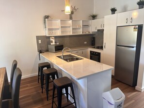 A modern kitchen with a central island, bar stools, a refrigerator, and built-in cabinets. - Sun-Set Satinay at Kingfisher Bay Resort (Kingfisher Bay)