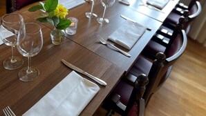 Una mesa de comedor dispuesta con copas de vino, cubiertos y un florero con flores.