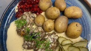 Un plato con albóndigas, patatas, pepinillos y salsa de arándanos.