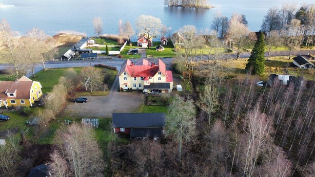 Una casa grande con techo rojo, rodeada por un lago pequeño y árboles.