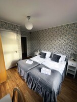 Un dormitorio con una cama doble, dos mesitas de noche, un buró, una silla y una puerta.