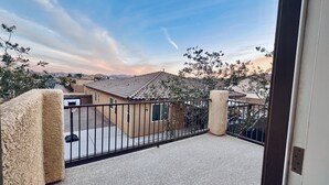 Un balcon donnant sur un quartier résidentiel, une clôture en métal et un ciel dégagé.