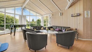 A spacious room with a high ceiling, a wooden wall, and a large window offering a view of greenery outside. - 4 bedroom gorgeous home in Børkop (Børkop)