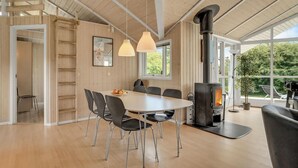 A spacious dining area with a large table and chairs, a wood-burning stove, and large windows offering views of greenery. - 4 bedroom gorgeous home in Børkop (Børkop)
