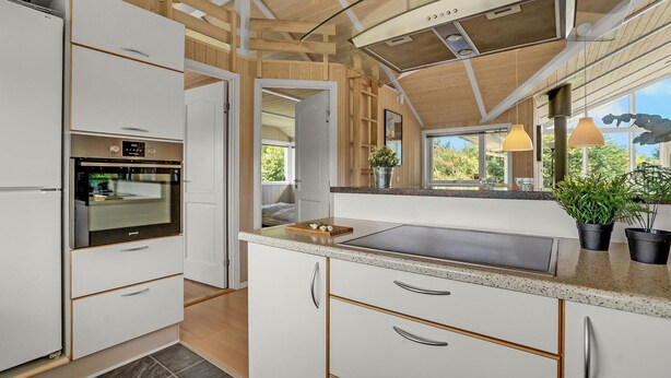 A modern kitchen with white cabinetry, a built-in oven, and a large window offering a view of greenery. - 4 bedroom gorgeous home in Børkop (Børkop)