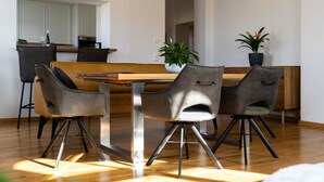 Un espace repas moderne avec une table en bois et quatre chaises, une plante en pot et une cuisine en arrière-plan.