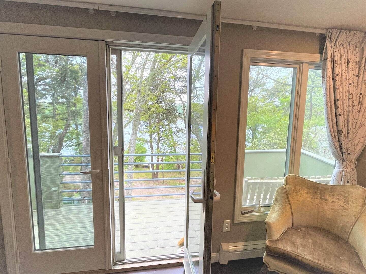 A room with a sliding glass door leading to a balcony, a cushioned armchair, and a window with curtains.