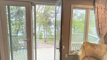 A room with a sliding glass door leading to a balcony, a cushioned armchair, and a window with curtains.