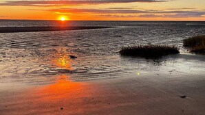 Un coucher de soleil sur une plage, où l’on peut voir des empreintes de pas dans le sable.