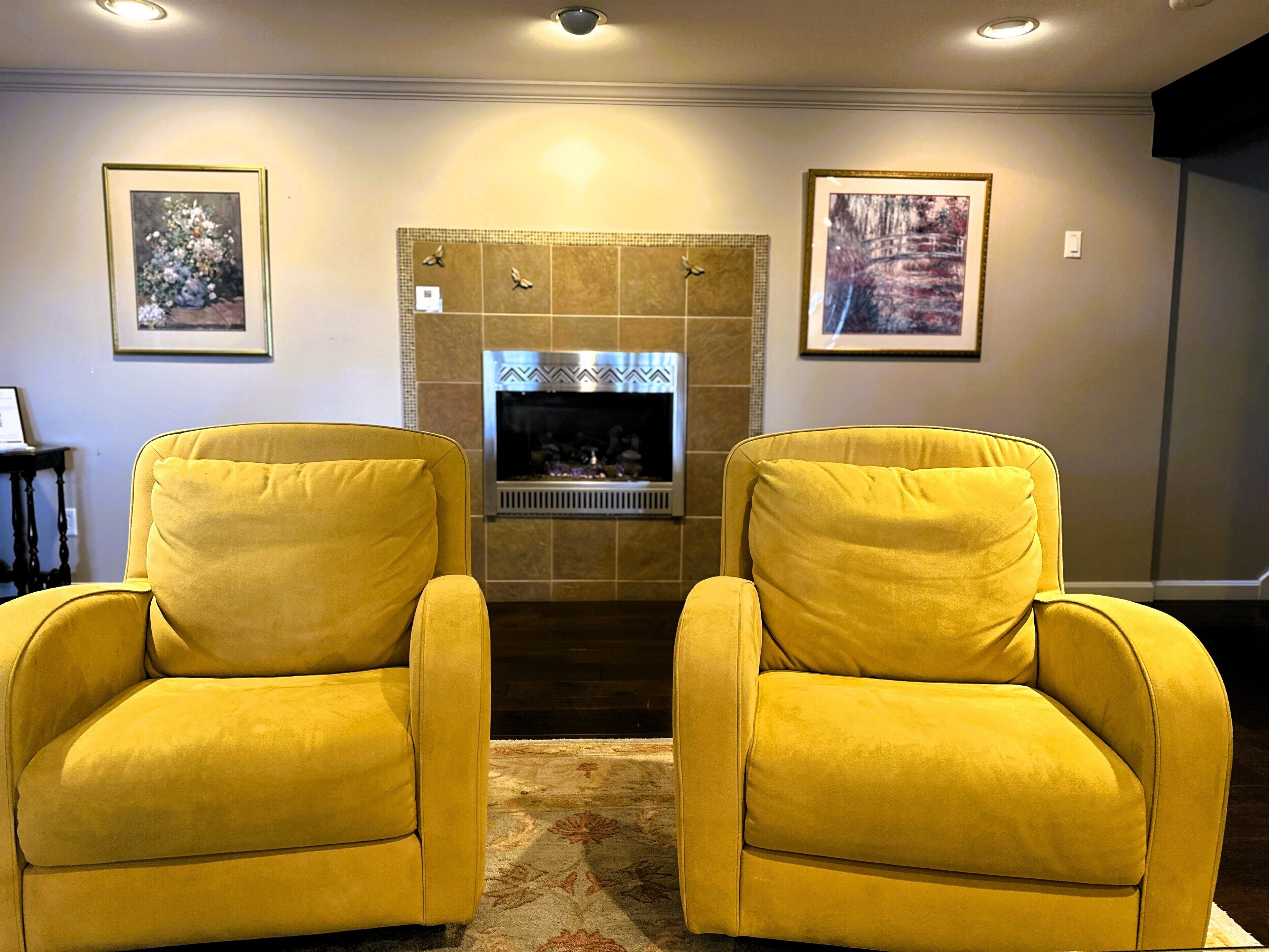 Un salon avec deux fauteuils jaunes, une cheminée et deux tableaux encadrés accrochés au mur.
