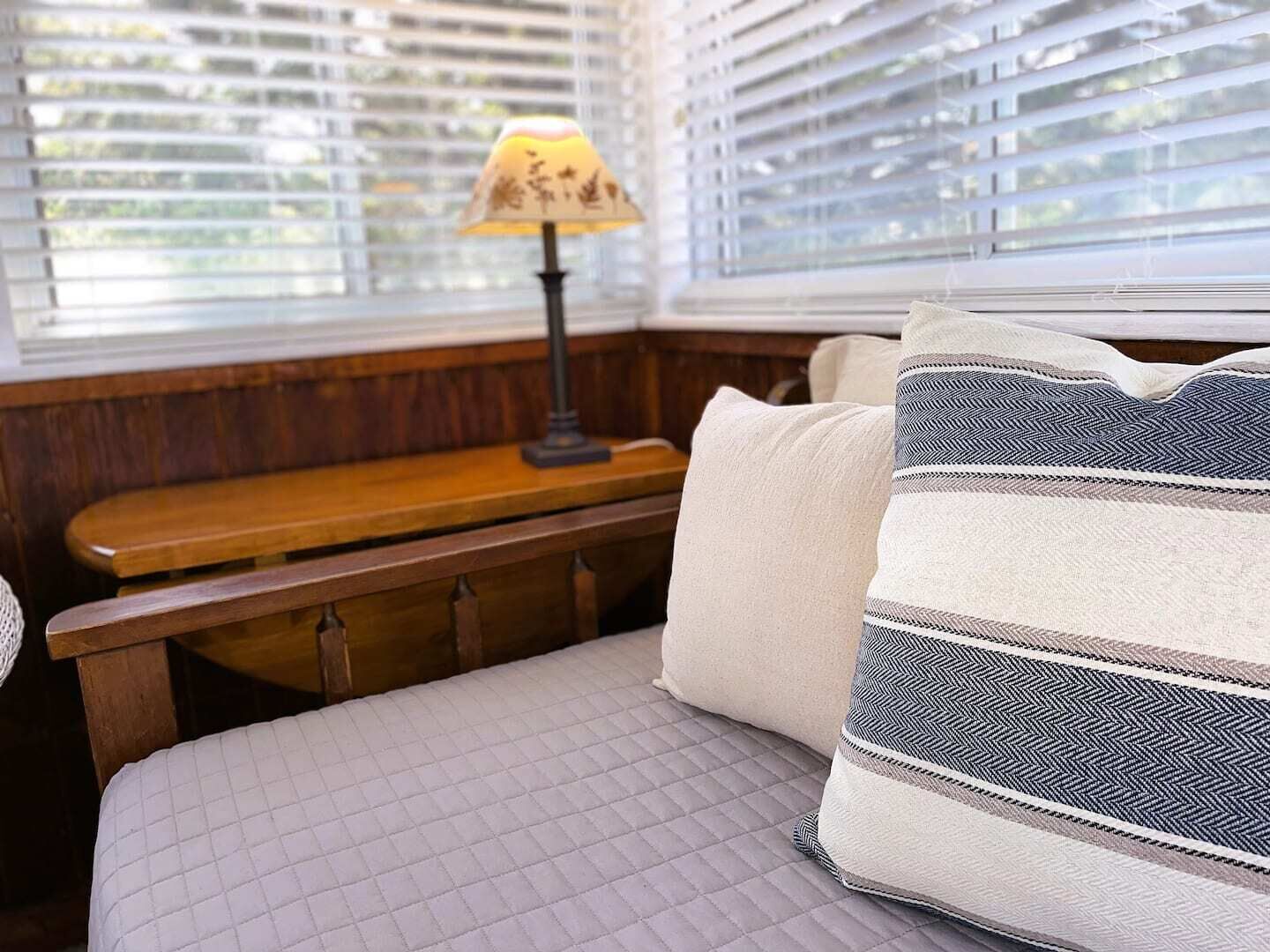 Uma cama com cobertura acolchoada, um banco de madeira e um abajur com padrão floral.