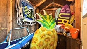 Une pièce en bois avec un ventilateur de plafond, un hamac, un grand ananas gonflable et une planche de surf.