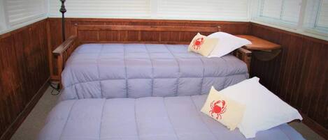 Una habitación con dos camas, paneles de madera, una lámpara y una ventana con persianas.