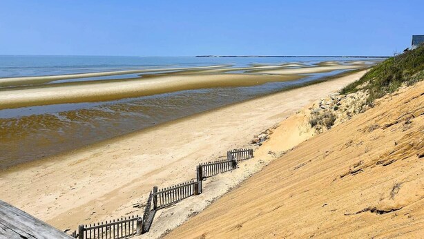 Une plage avec une promenade en bois et une clôture menant à un bâtiment.