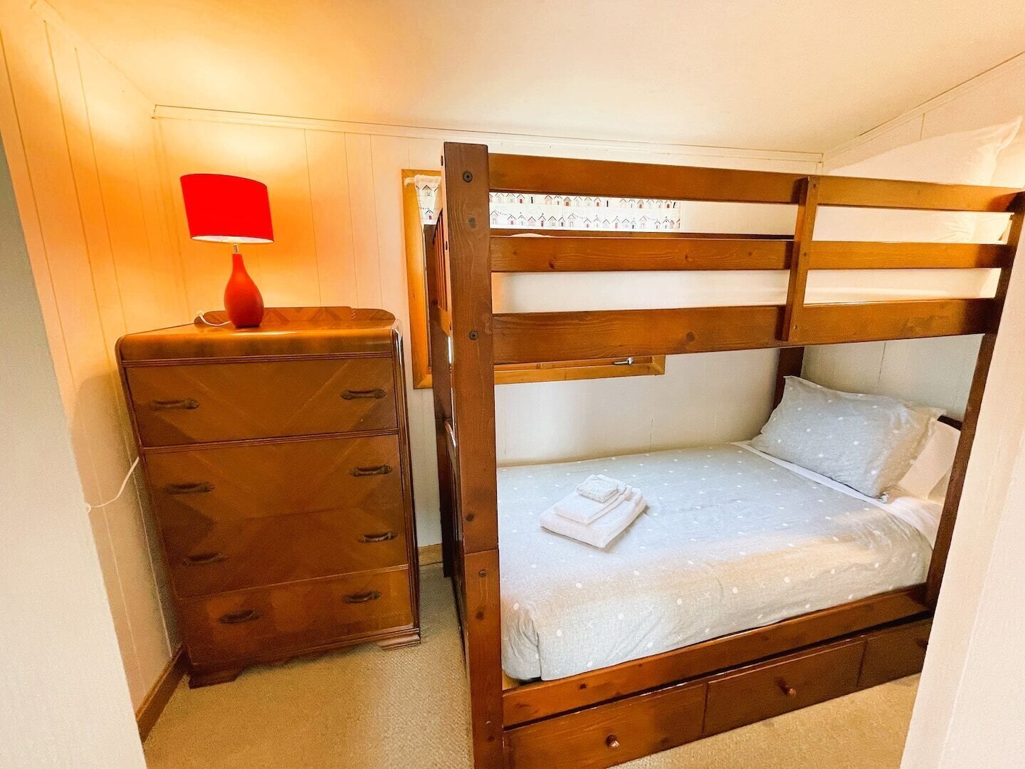 Une petite pièce, de taille modeste, comprenant un lit superposé, une commode et une lampe.