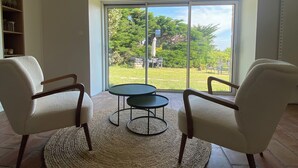 Una habitació àmplia amb dues butaques blanques, una taula rodona petita i una finestra gran que ofereix vistes a un jardí.