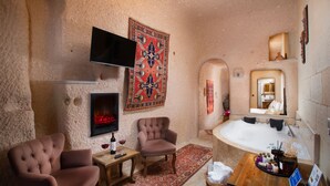 A cozy room with a fireplace, two armchairs, a TV, and a large bathtub. - Simera In Cappadocia - Special Class (Nevsehir)