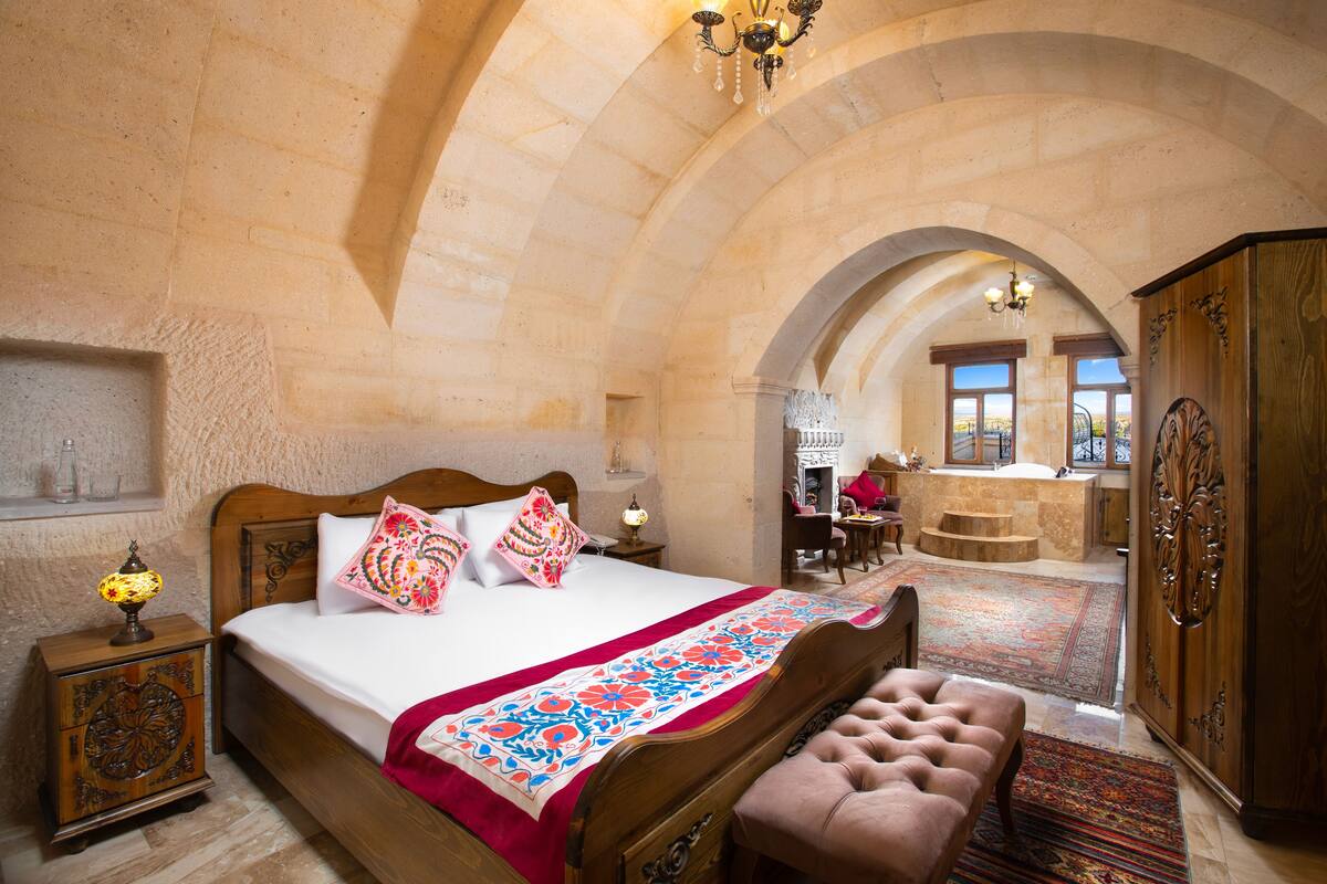 A spacious bedroom with a large bed, a wooden bench, and a view of the terrace.