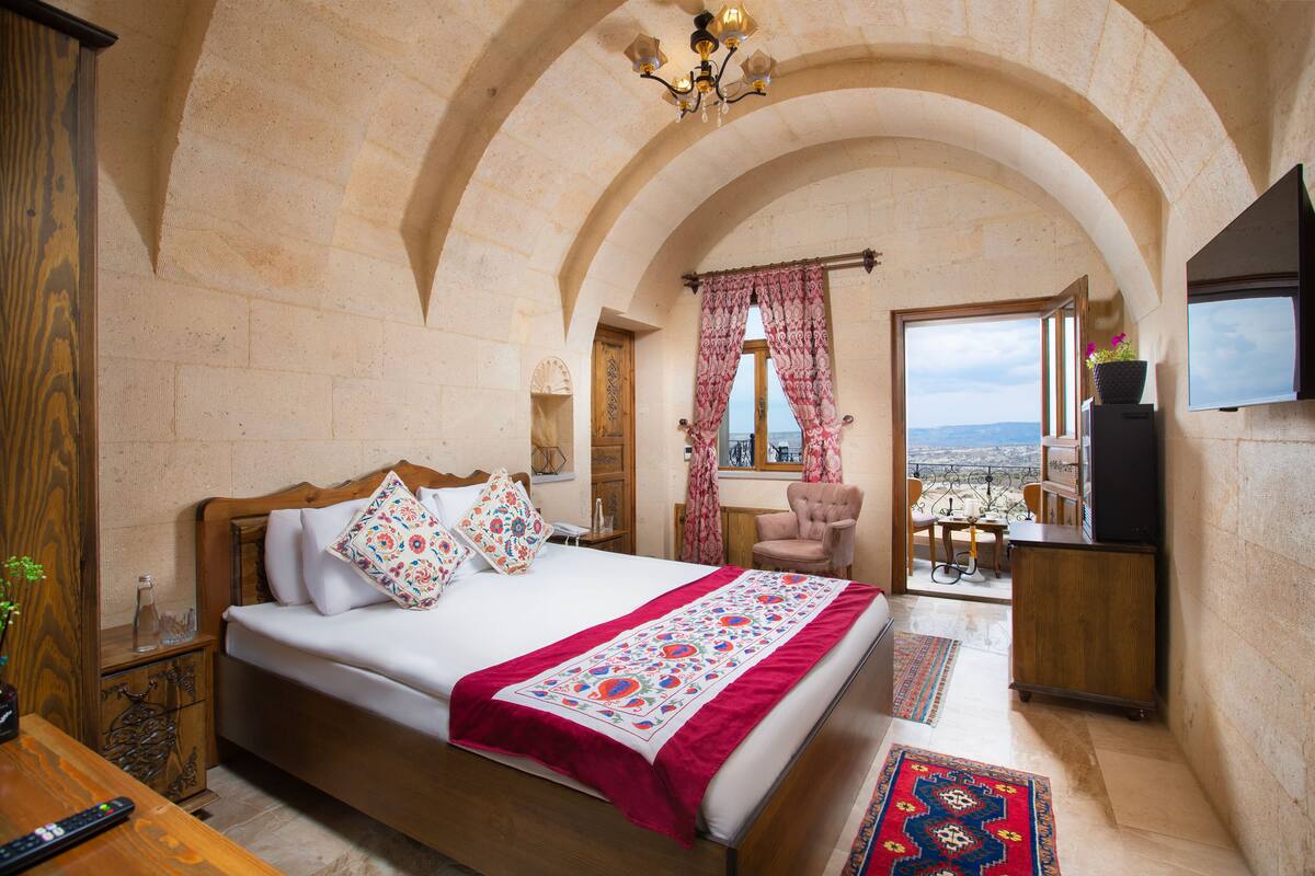 A bedroom with a large bed, a wooden nightstand, a TV, and a view of the city.