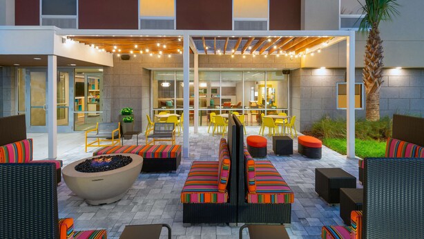 An outdoor patio area with seating arrangements, a fire pit, and string lights. - Home2 Suites by Hilton Wildwood the Villages (Wildwood)