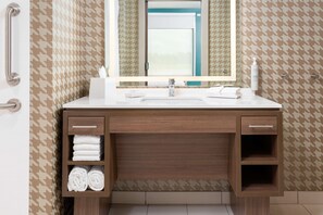 Une salle de bain avec un mur orné d’un motif à carreaux, un meuble-lavabo en bois avec un miroir, un évier et des étagères avec des serviettes.
