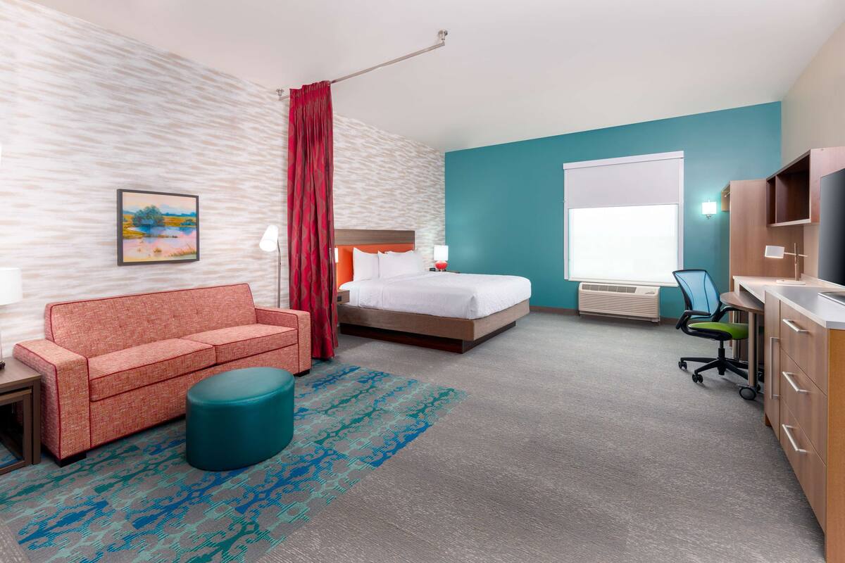 A hotel room with a bed, a sofa, a desk, and a chair.