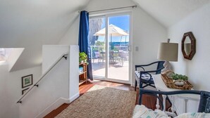 Quarto com escada, uma grande porta de vidro deslizante que dá para um pátio exterior, uma cadeira de vime e uma pequena mesa com uma cesta.