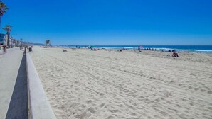 Uma extensa praia de areia com uma torre salva-vidas, guarda-sóis e pessoas relaxando.