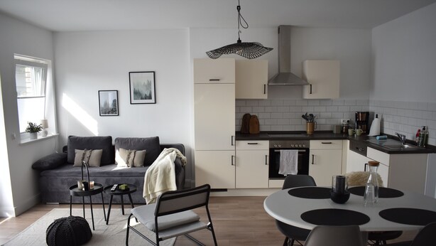 A modern kitchen with white cabinets, a dining table with chairs, a sofa, and a small side table. - Beautiful vacation apartment near Pietzmoor (Schneverdingen)